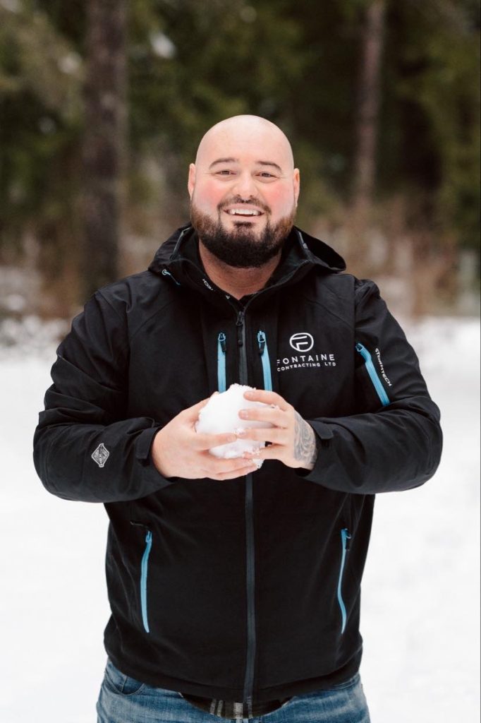 Man smiling about holding a snowball outdoors in a snowy environment.