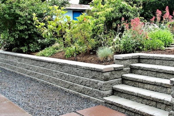 A stone retaining wall with plants and a blue house.